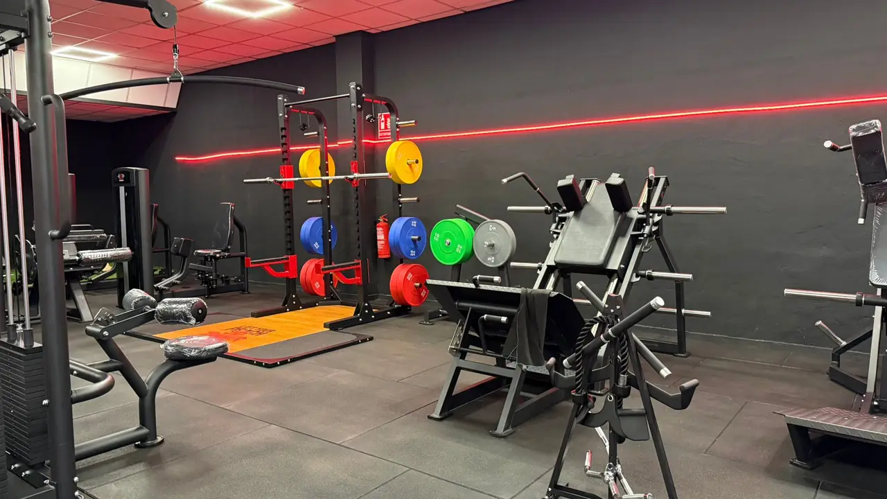 Máquinas de fuerza de carga libre y rack con discos de colores junto a la línea de luz roja de la sala