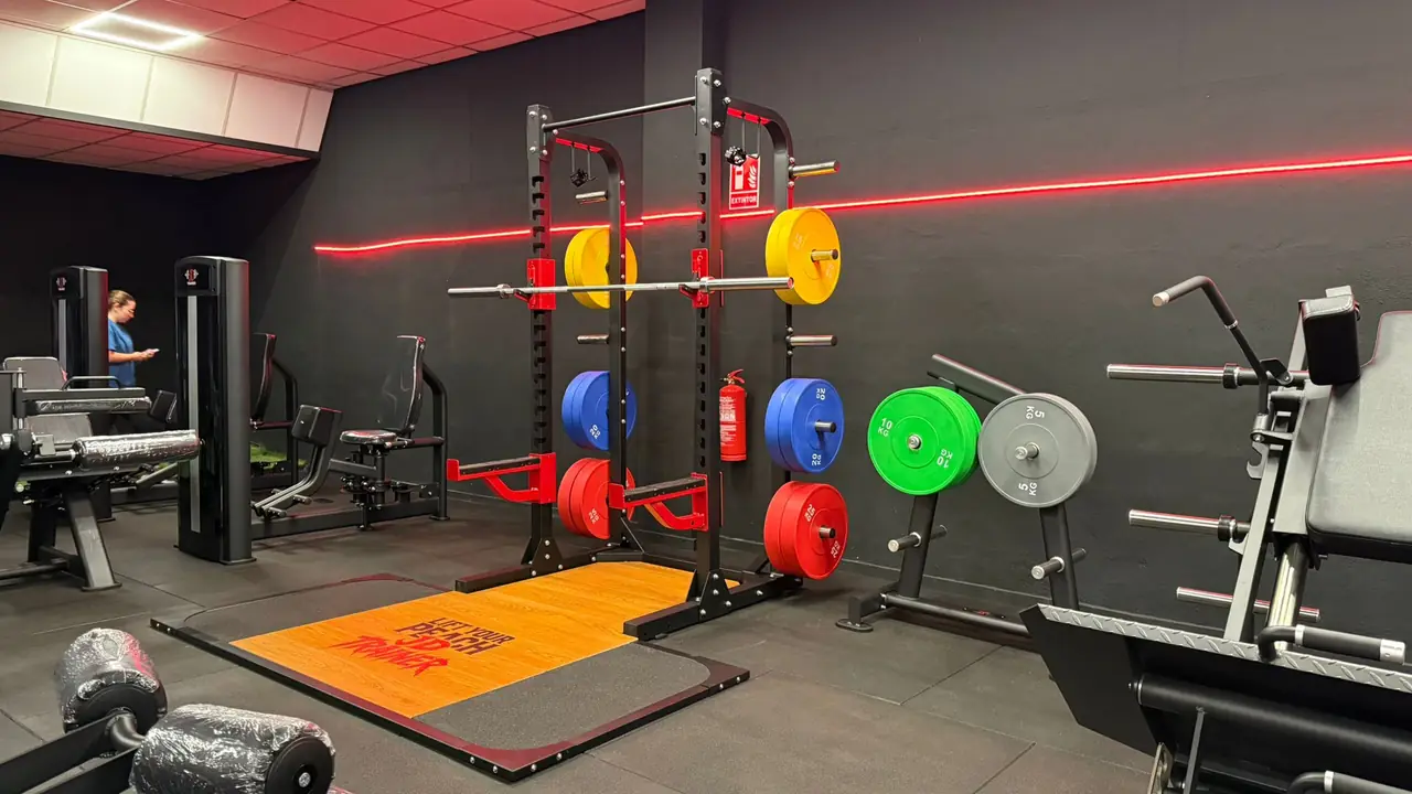Rack de sentadillas con discos olímpicos de colores sobre plataforma naranja en JD Trainer